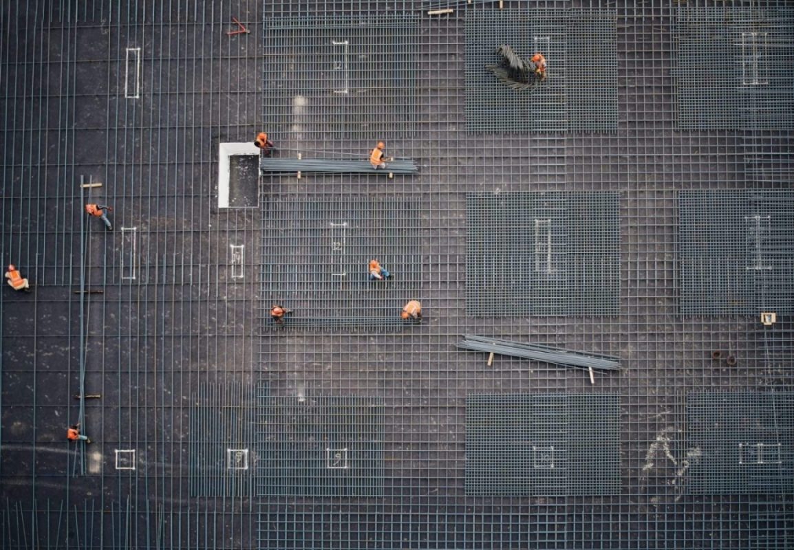 A wide photo from above of workers, working on a woof.