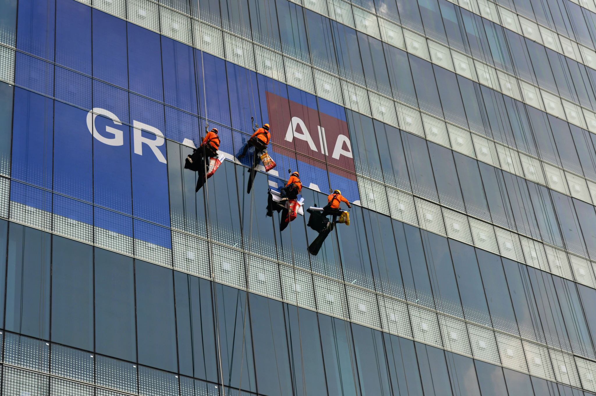 4 men handing on ropes cleaning the side of a building.